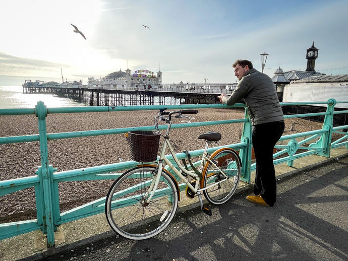 Mann, der mit einem Fahrrad an einem Geländer am Meer lehnt