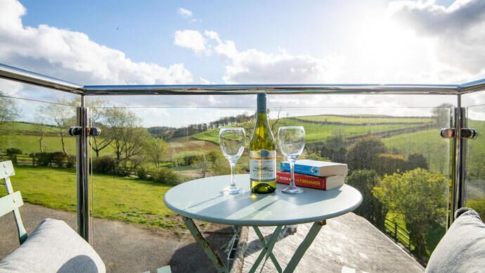 View from the balcony with a bistro table and chairs set with two novels, two wine glasses and a bottle of wine with a rural landscape in the background.