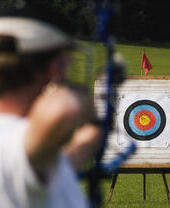 A person aiming a bow and arrow at a target from distance.