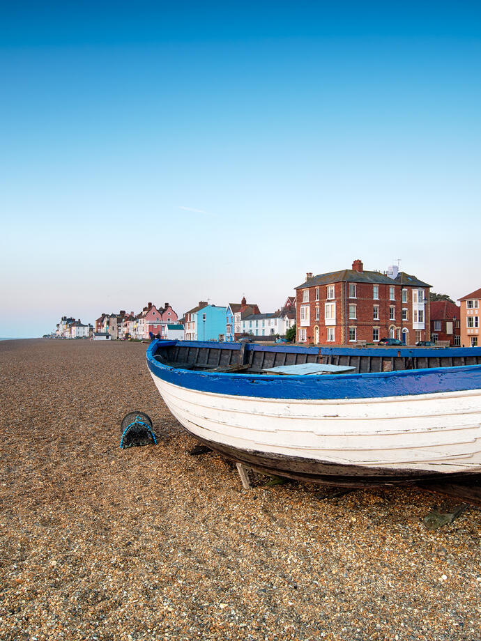 Wooden boat on a pebble beach with colorful houses and clear sky in the background, coastal town scenery.