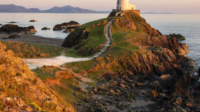 A path leading to a lighthouse on a prominent rocky outcrop by the sea