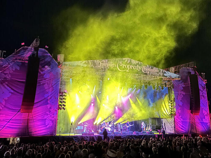 A crowd of people in front of the stage of a musical festival at night. 