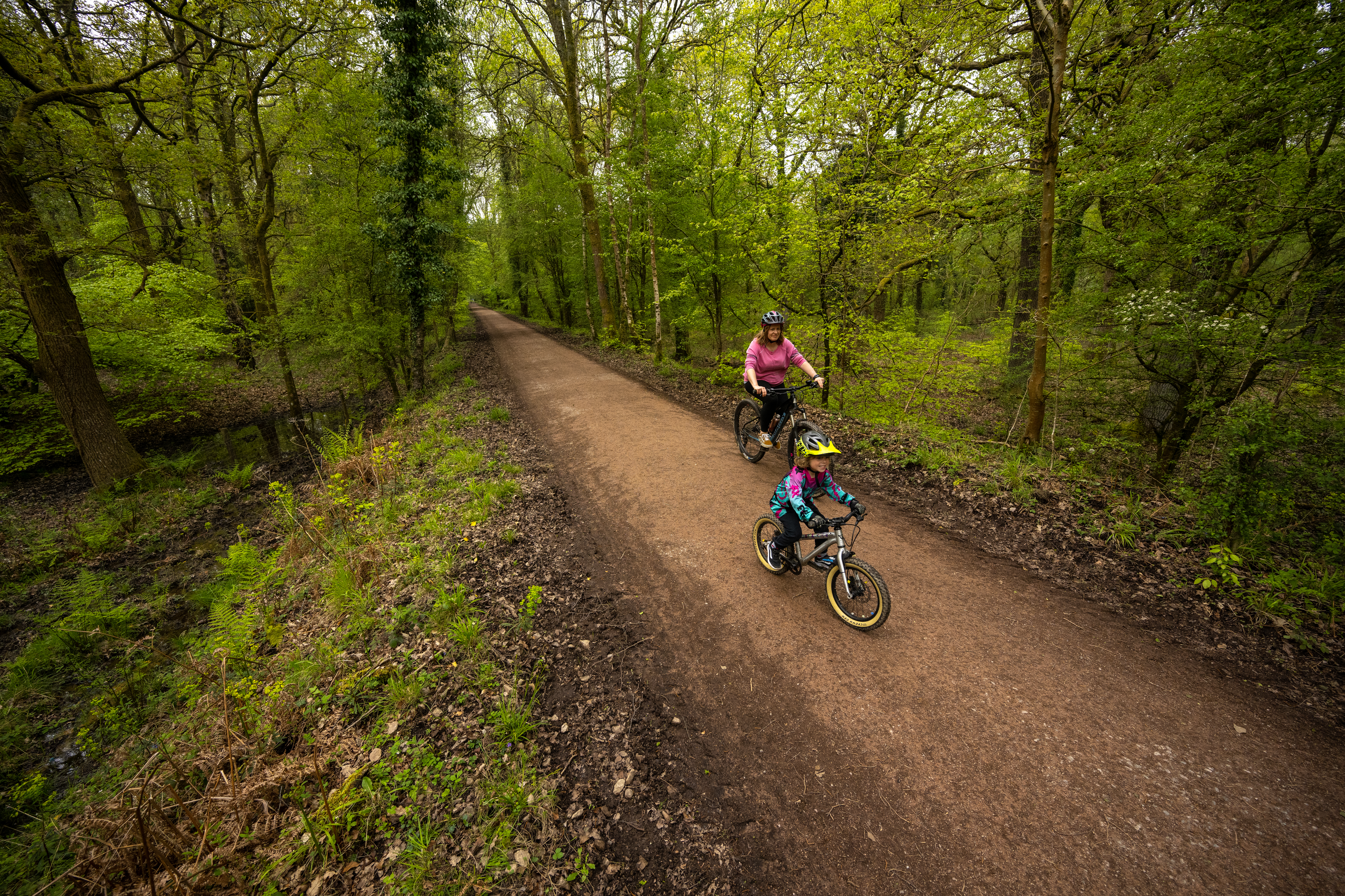 Mother and son riding through trees along a forest path.