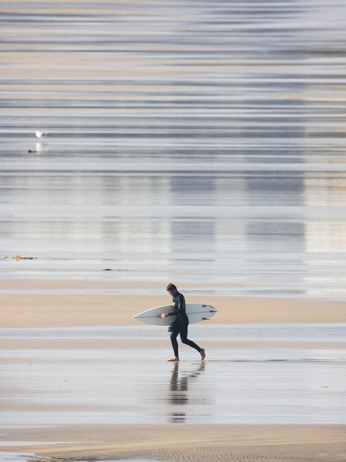 Surfer walking out of the sea holding a surfboard and wearing a wetsuit