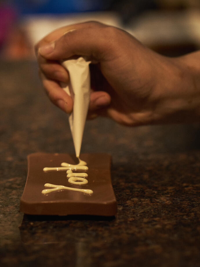Person decorating dark chocolate with white chocolate piping