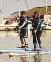 Man and woman on stand up paddle boards with boats in the background