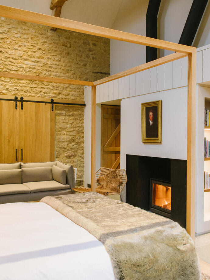 Cozy modern bedroom with stone wall, wood accents, fireplace, bookshelf, sofa, desk, and soft lighting. Inviting and stylish interior.