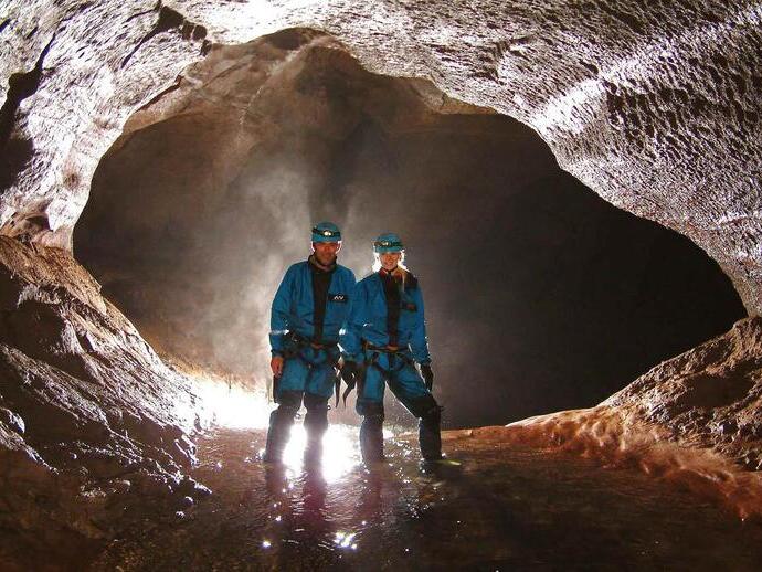 A couple standing in ankle-deep water within a back lit cave