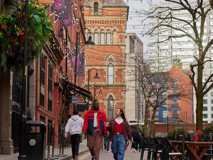 Two men chatting and walking down a street with cafes and a canal.
