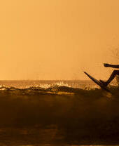 Silhouette eines Mannes, der bei Sonnenuntergang im Meer surft.