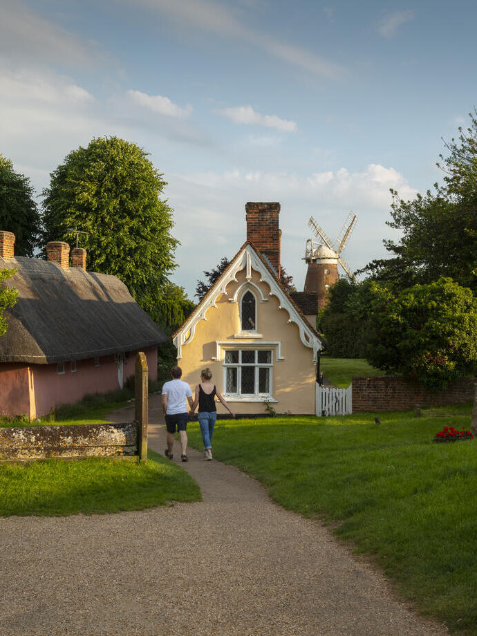 A man and a woman walk toward thatched cottage and a windmill