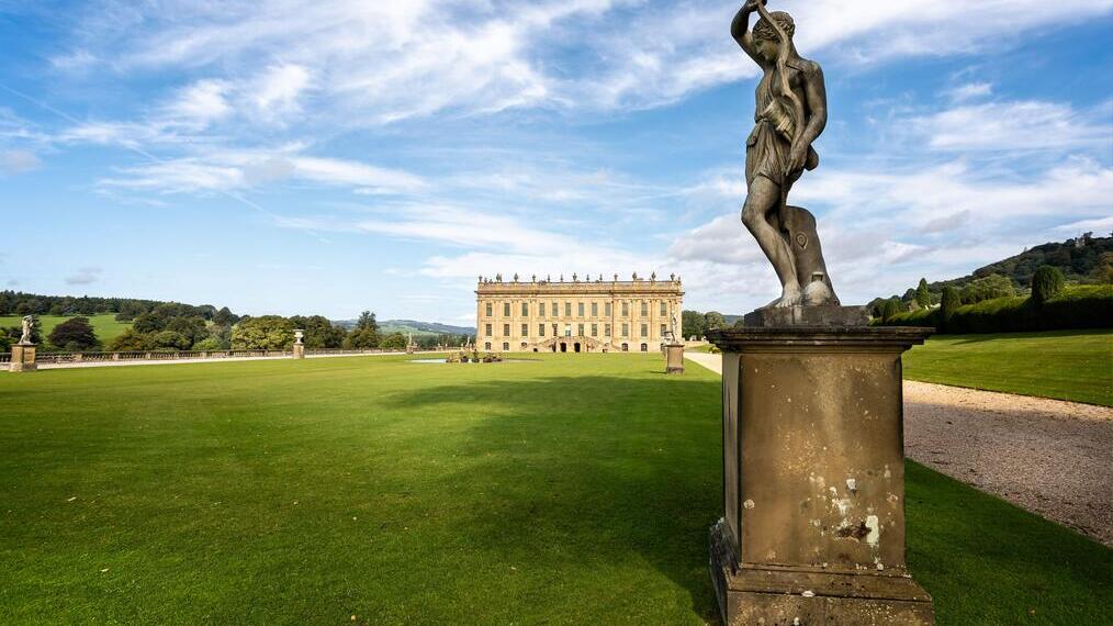An ornate statue outside a magnificent mansion on flat green lawns