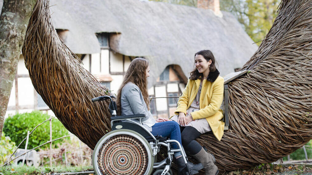 Female wheelchair user and friend sat on a wicker sculptured seat