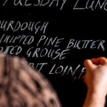 Close up of human hand writing menu on blackboard