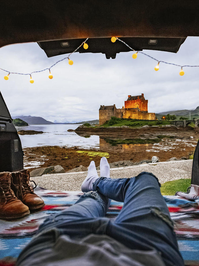 Mann liegt in einem Wohnmobil und schaut auf eine Burg in der Ferne