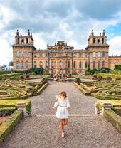 Woman walking through the formal gardens in front of a palace