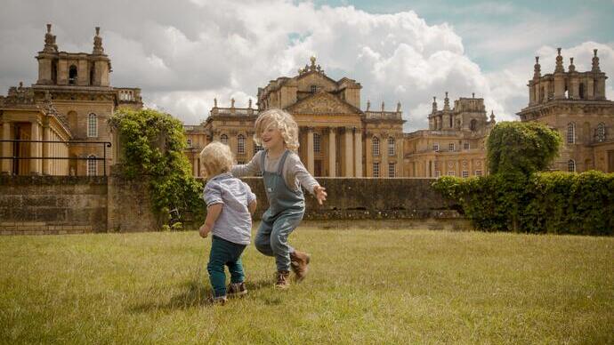 Two children play on the lawn in front of a palace