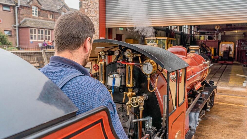 Hombre conduciendo una maqueta de locomotora de vapor hacia la cochera