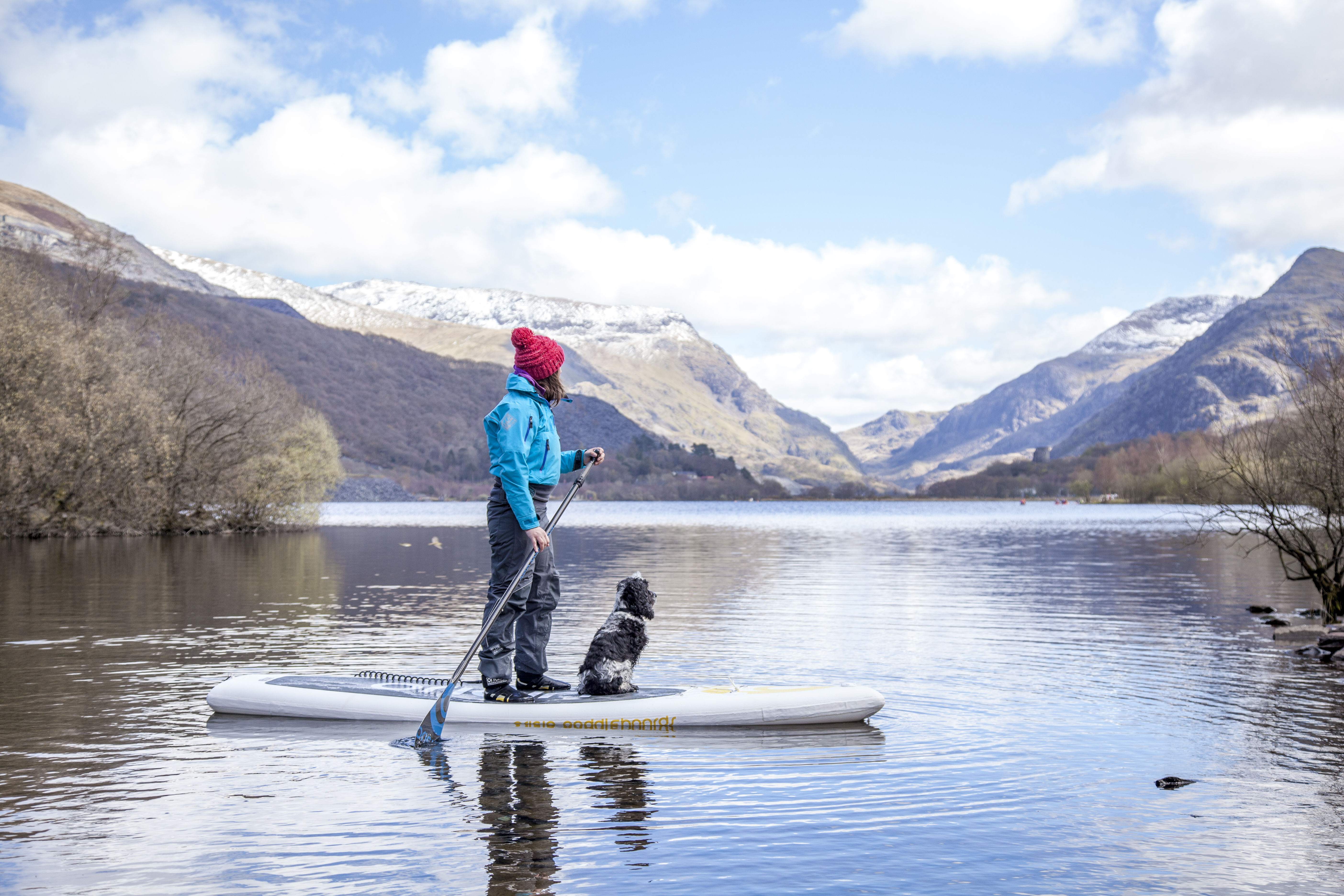 Woman and a dog on a paddleboard on a lake with mountains in the background