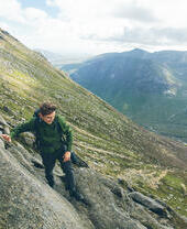 Man climbing to mountain summit in rugged mountains.