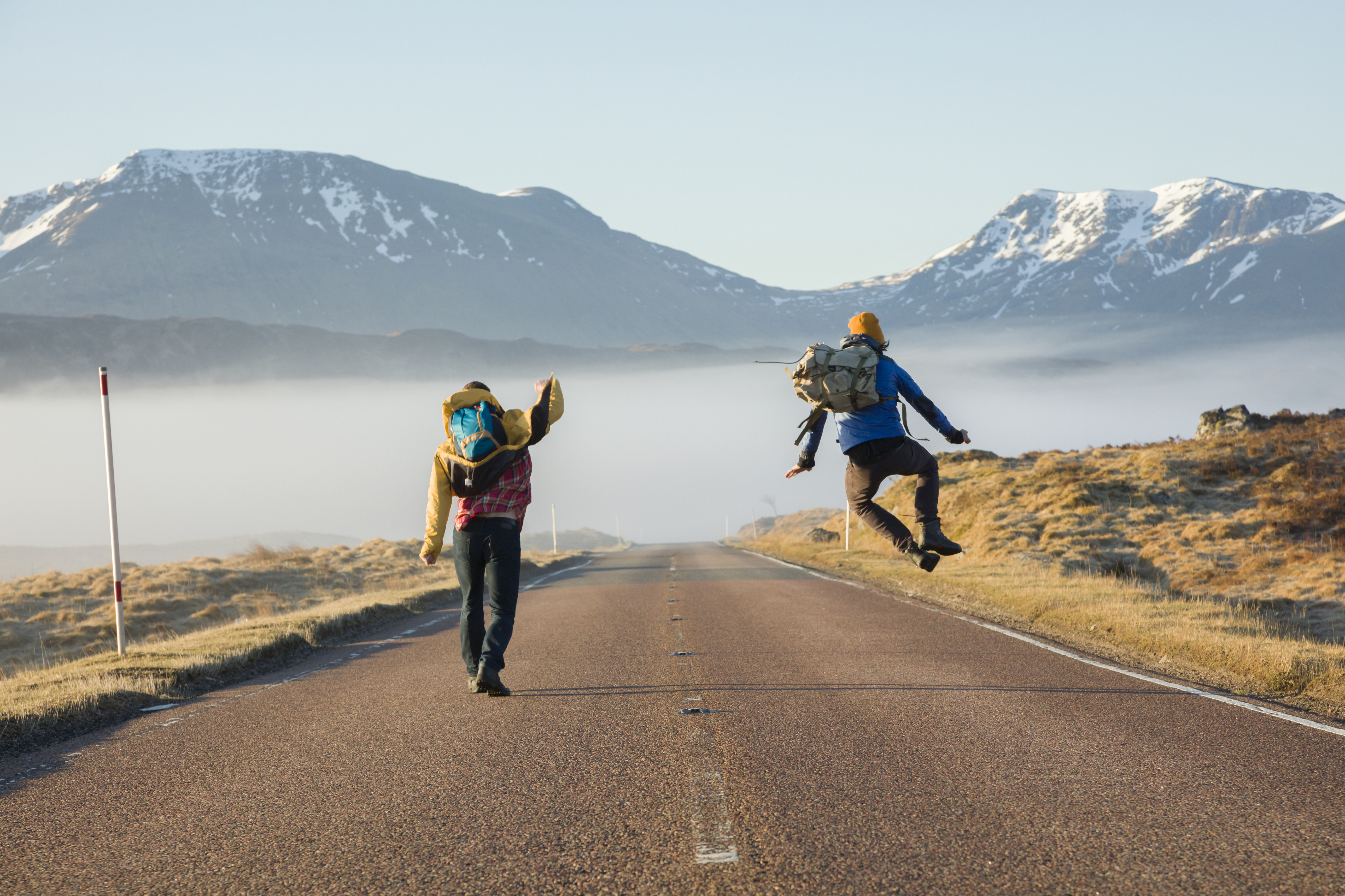 Two men walking and jumping on a road surrounded by mountains