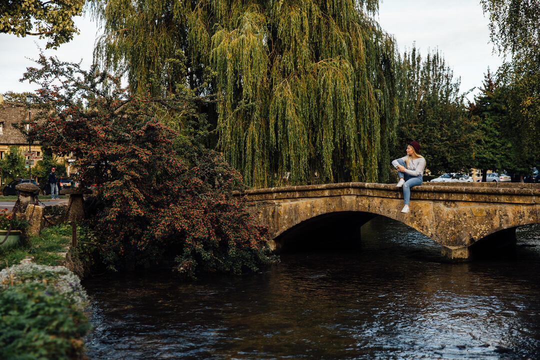 Femme assise sur un petit pont de pierre au-dessus d'une rivière dans un village