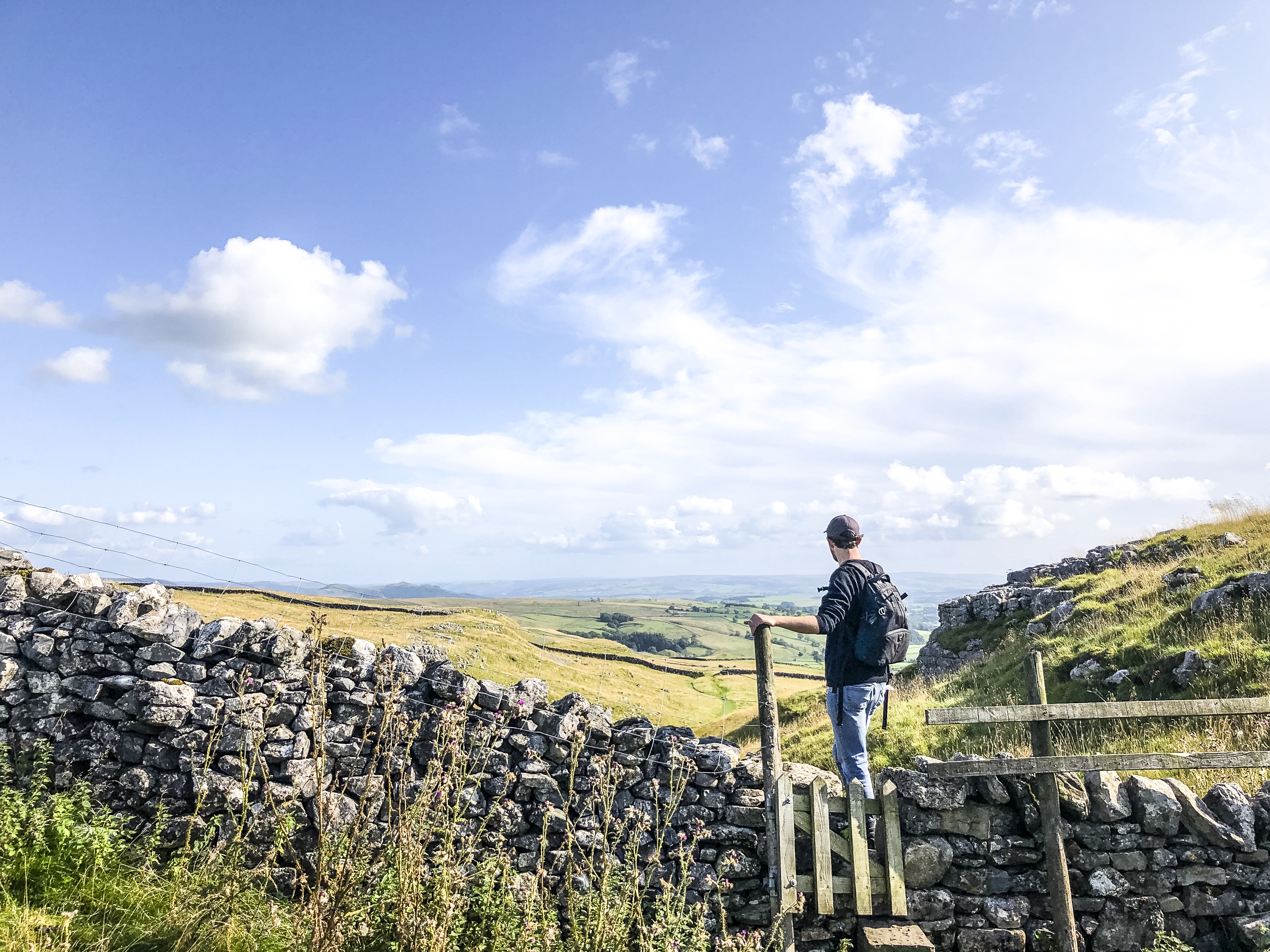 Man standing on stile over stone wall looking at landscape