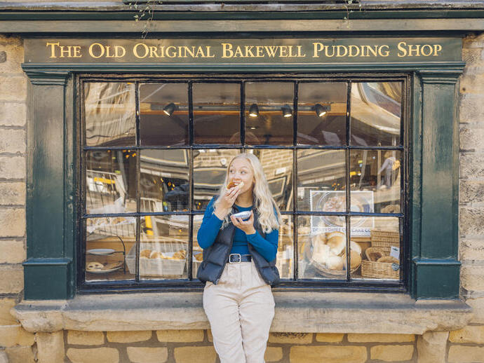 Woman eating bakewell tart in front of bakery