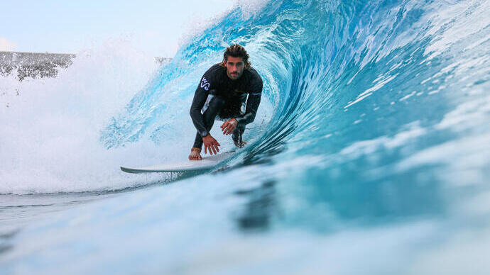 A surfer in a wetsuit riding inside a clear, blue wave.