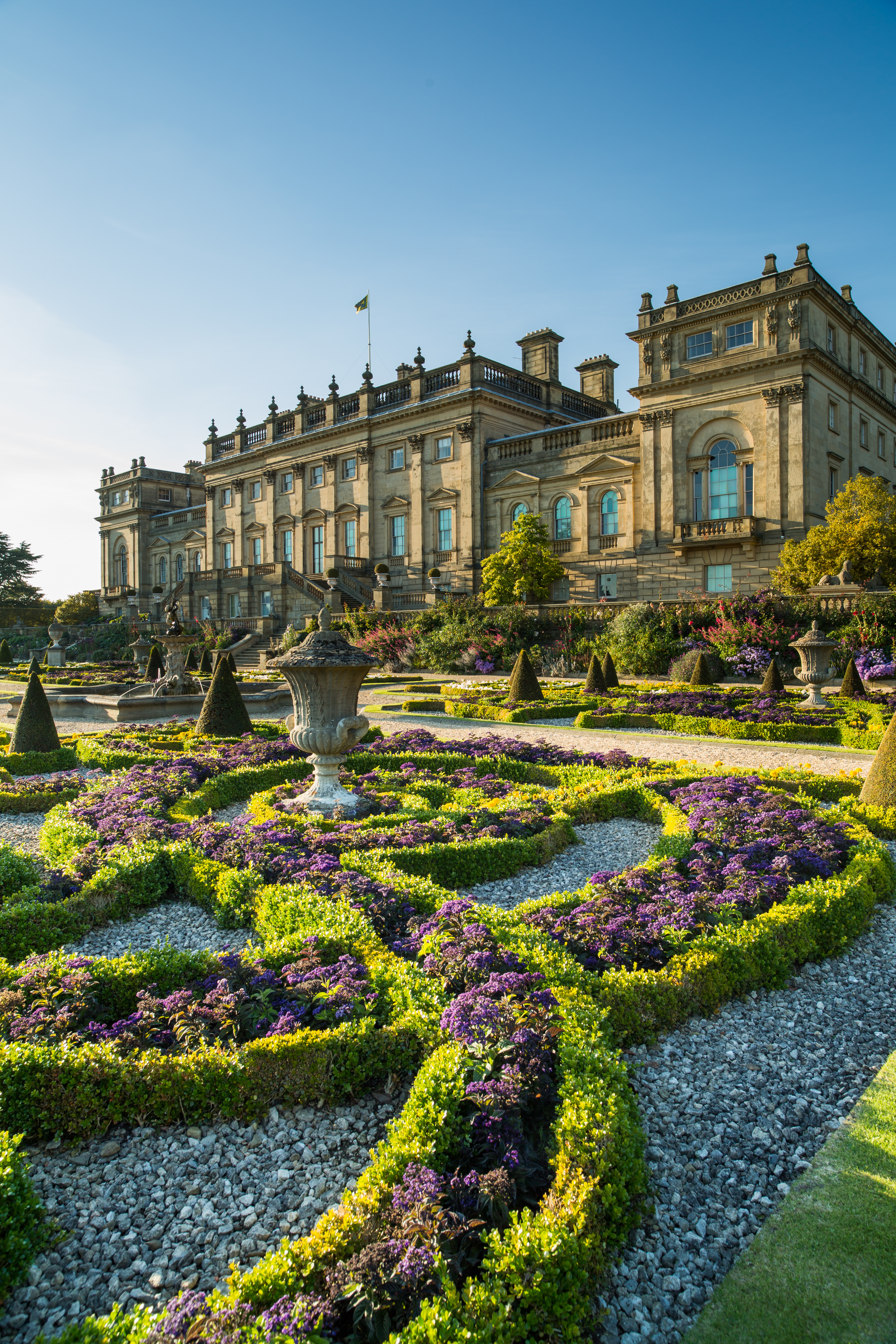 A formal garden with statues and low hedges in front of a stately house