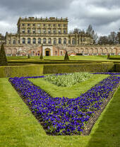 Beautiful manicured flower gardens and sculptured hedges in front of a large mansion.