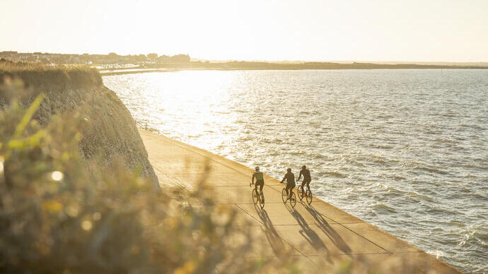 Tres ciclistas en un sendero costero durante la puesta de sol
