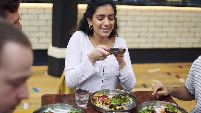 Femme assise avec des amis à une table, prenant une photo des plats dans une aire de restauration
