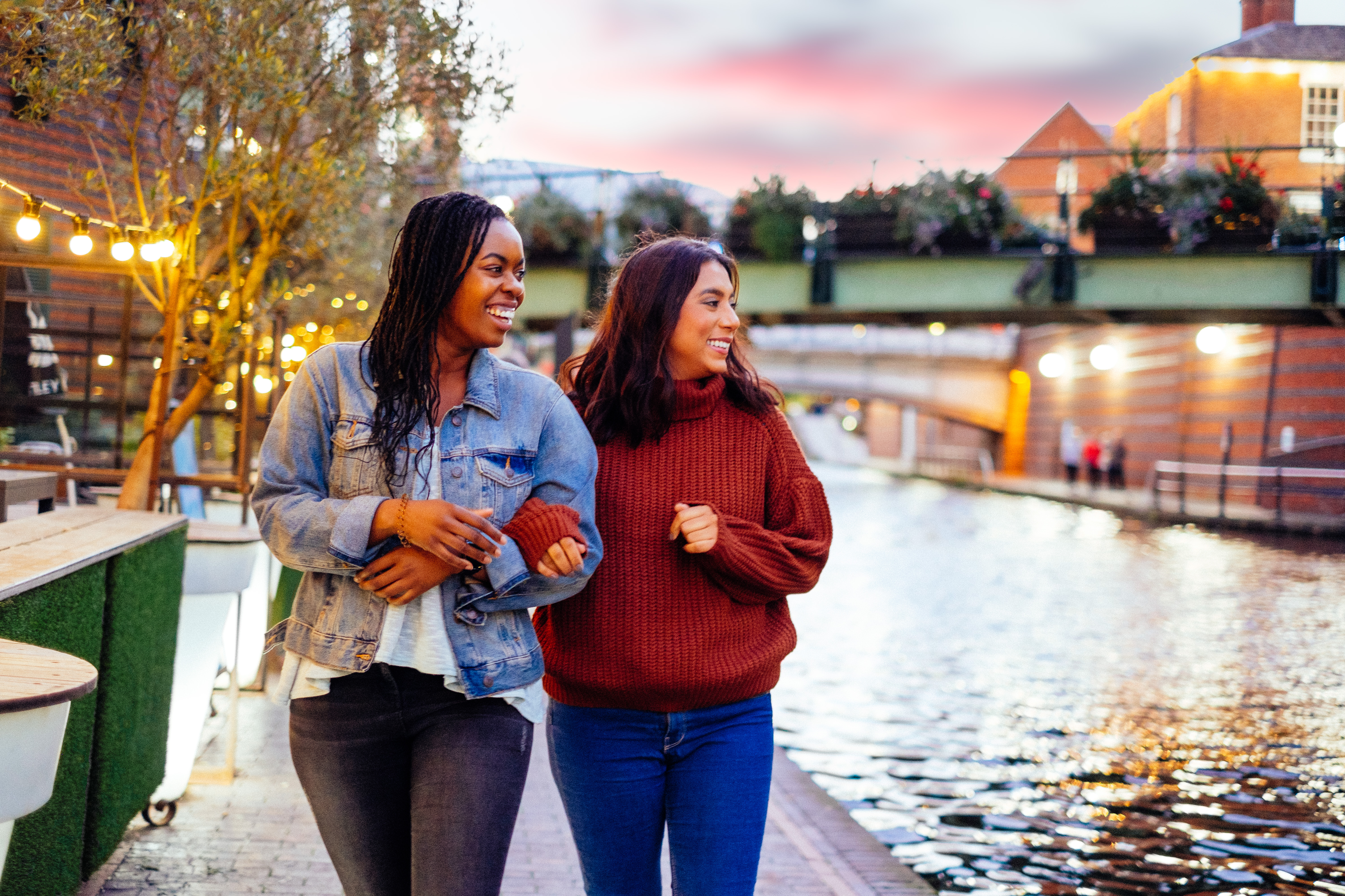 Two women, linking arms, walking beside a canal in evening