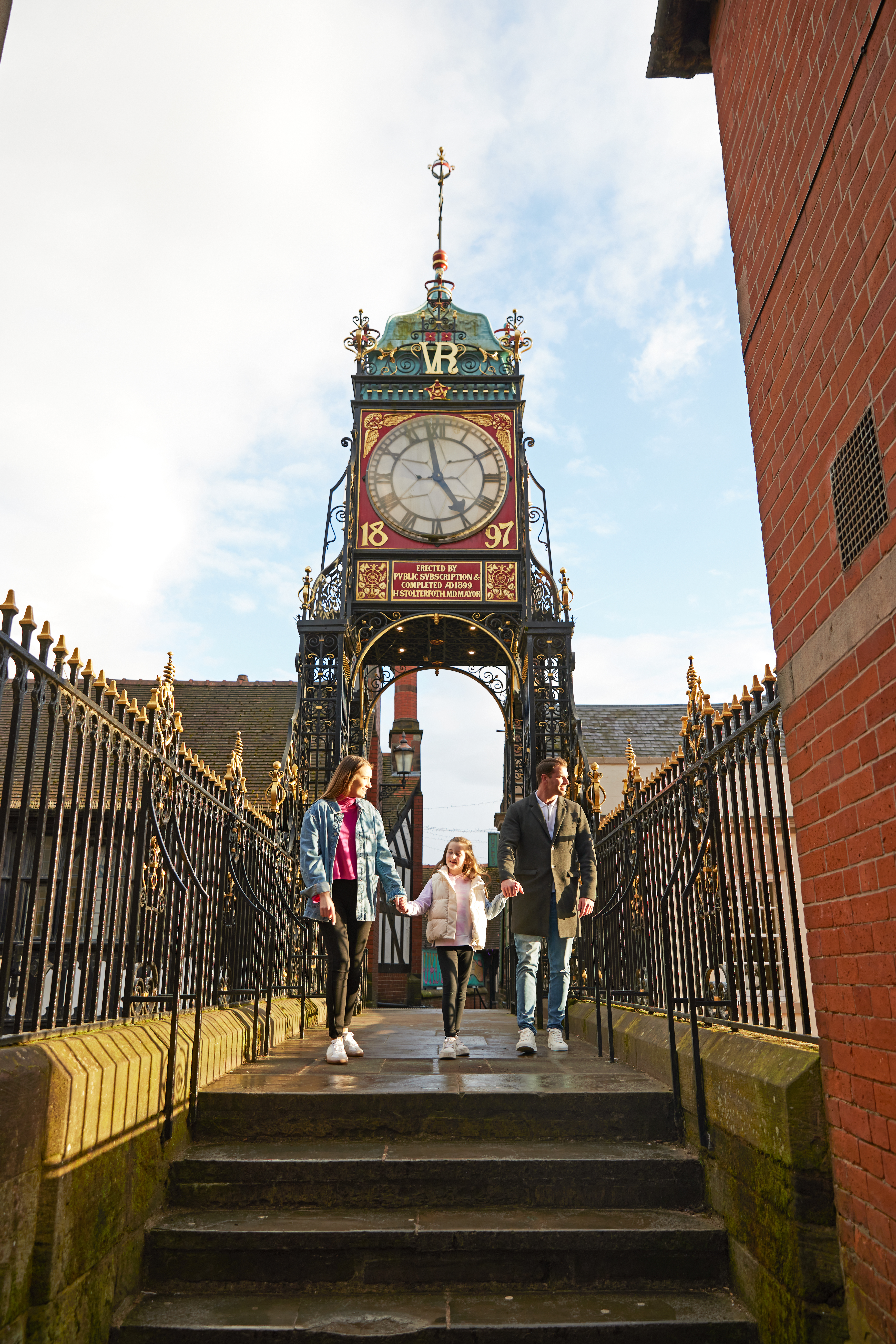 A family of three look out over a town from a clocktower bridge.