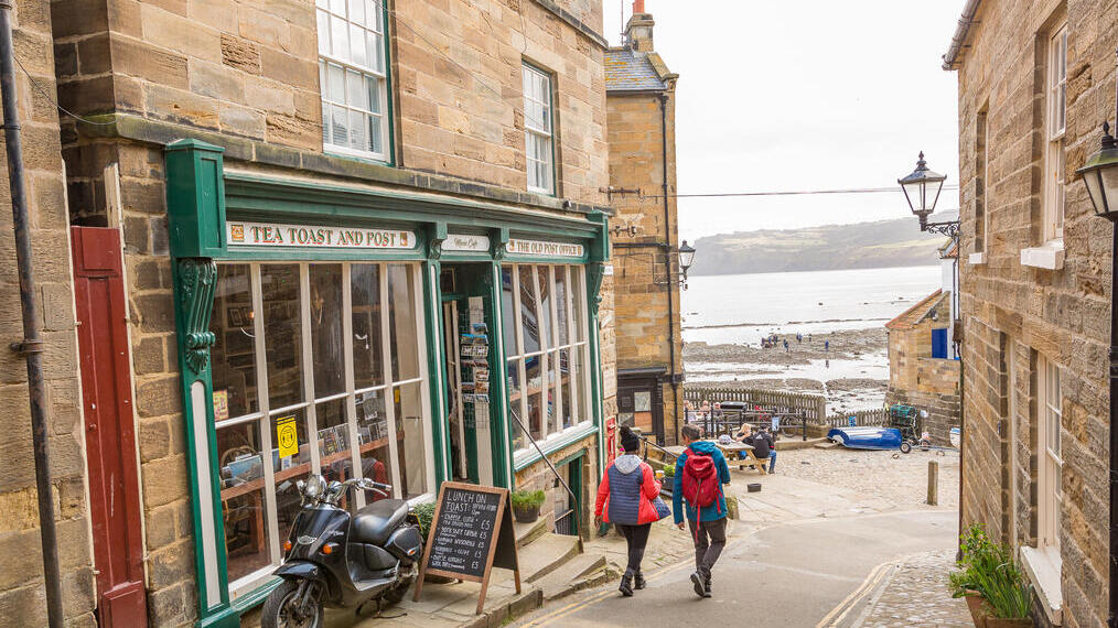 Paar spaziert eine schmale Straße entlang, im Hintergrund das Meer