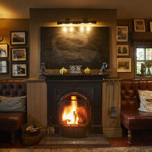 A fireplace in a pub with a lit fire flanked by two leather sofas with tables