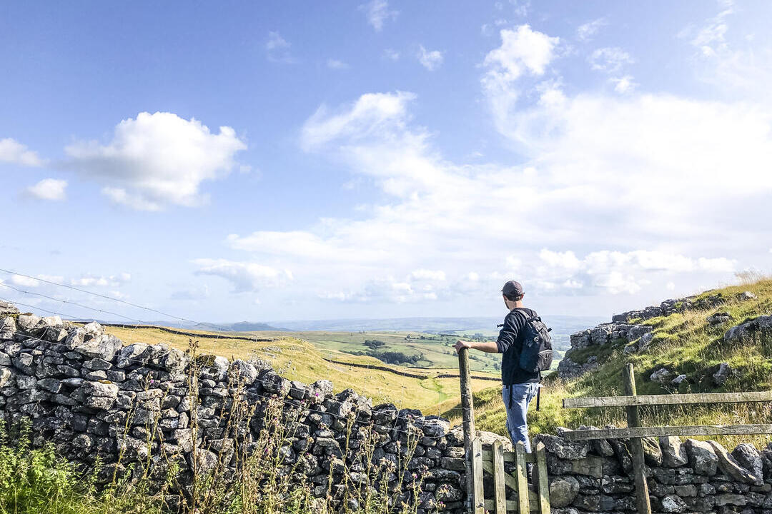 Man standing on stile over stone wall looking at landscape