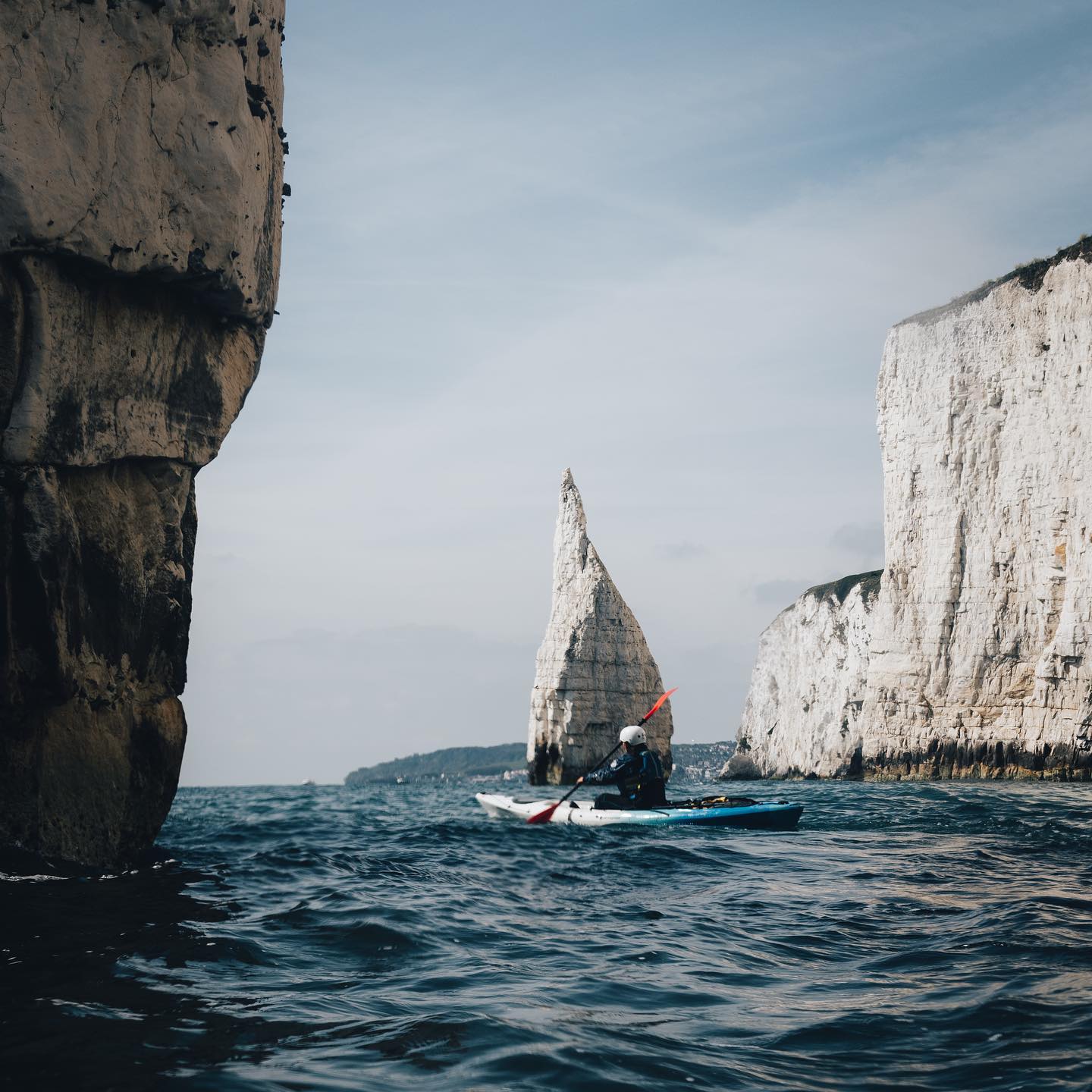 Person in canoe navigating coastline with cliffs in the background