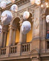 Two men looking at installation of suspended head sculptures inside a museum.