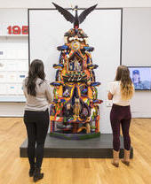 People admiring a sculpture of a totem pole in an art gallery.