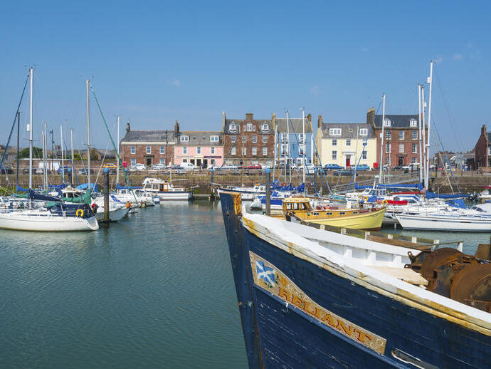 Harbor with sailboats and a large boat in foreground, colorful waterfront buildings under a clear blue sky.