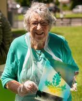 Mujer vestida de verde sosteniendo una obra de arte en una cafetería de la plaza