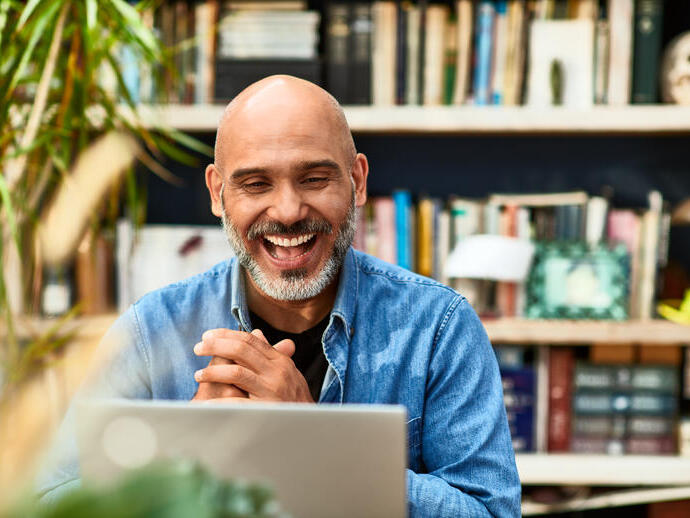 Cheerful handsome mature man at home speaking on video call using laptop