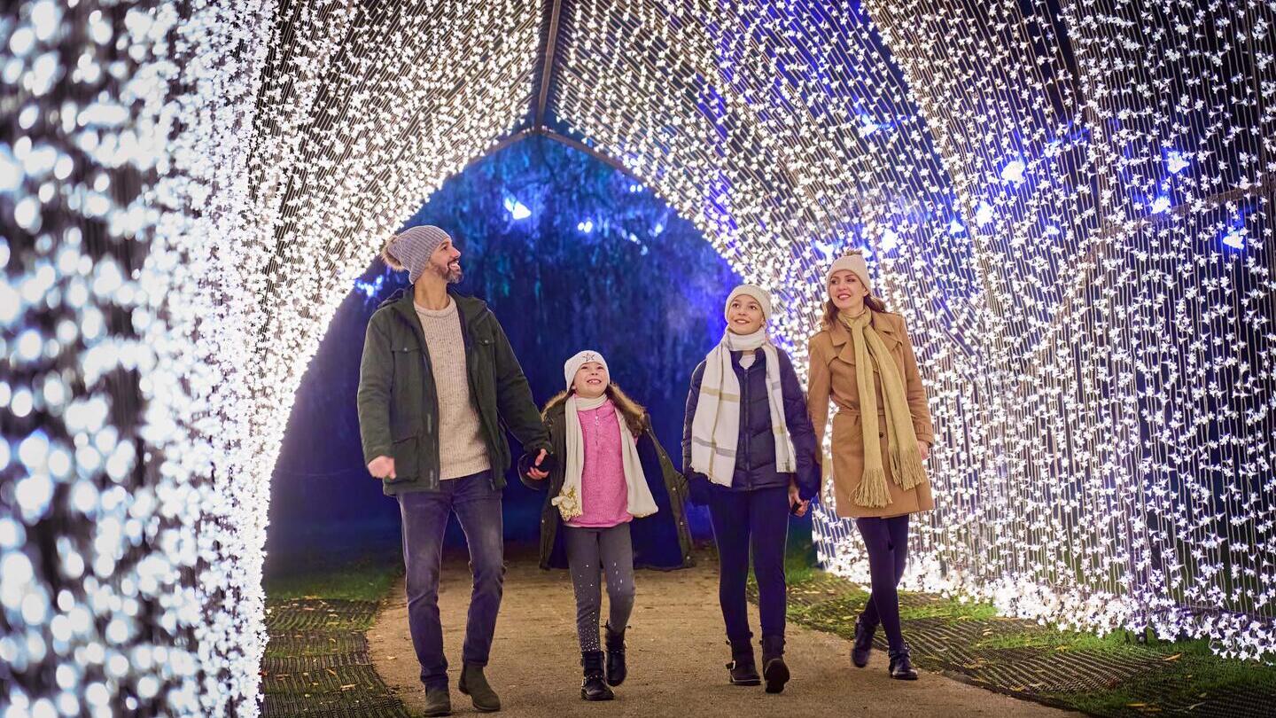 Family with children walk under a Christmas lights archway