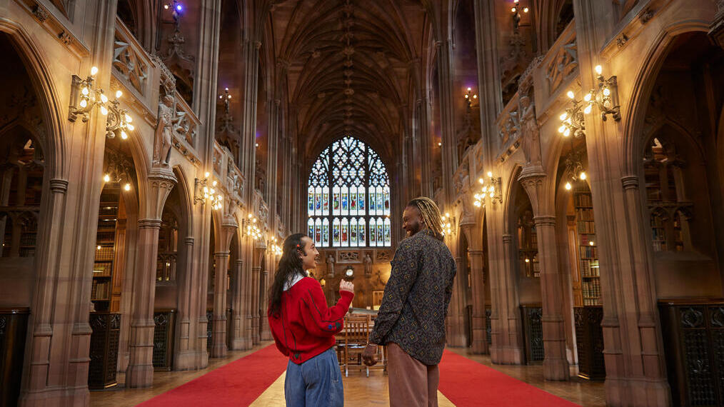 Two men chatting, exploring a large library.