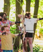 A family learn archery skills in a woodland setting