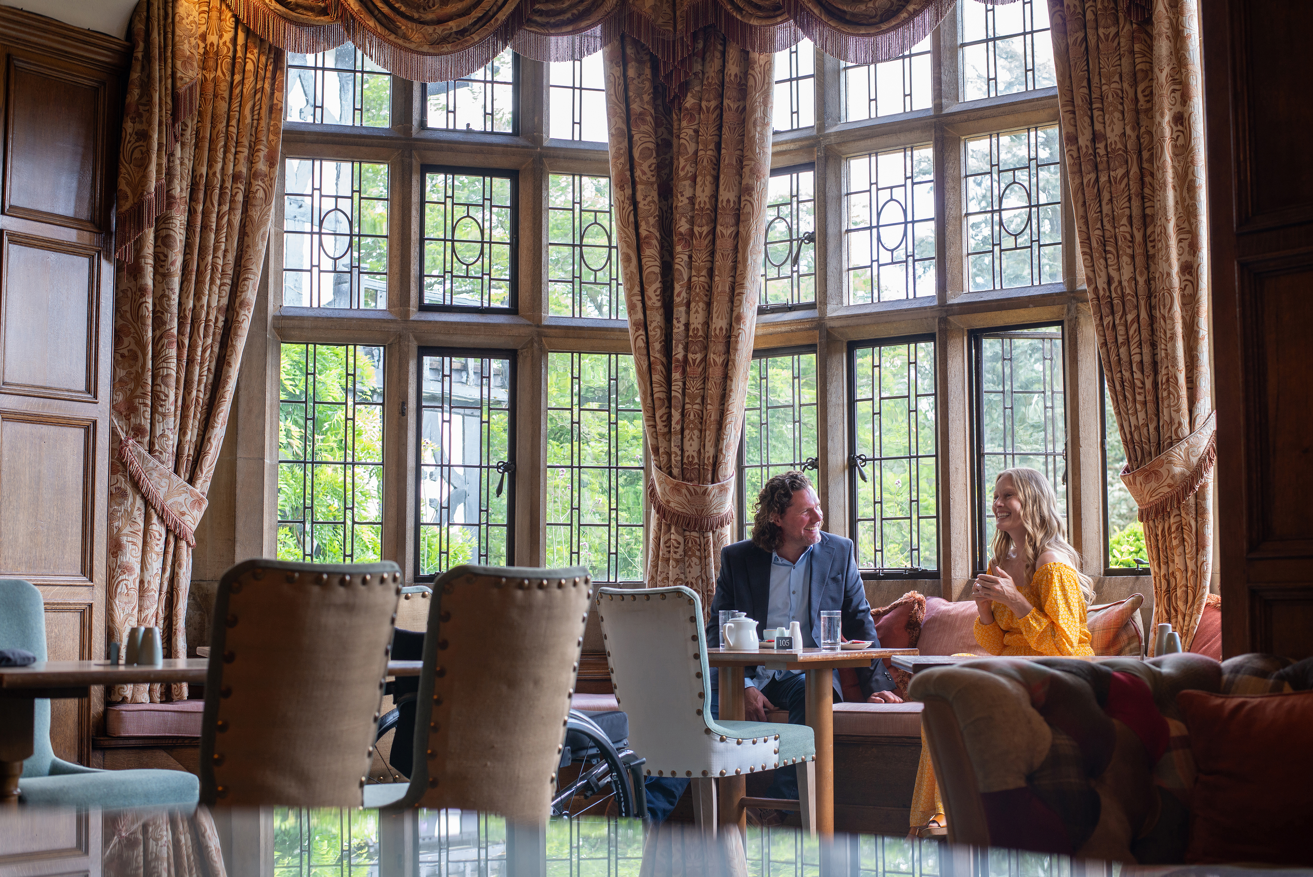 A man and a woman have coffee in a hotel lounge with large windows.