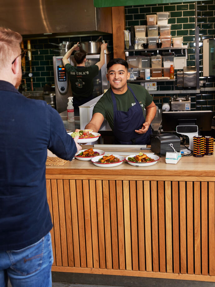 A wait staff member serves food and drink to a waiting customer at a local restaurant