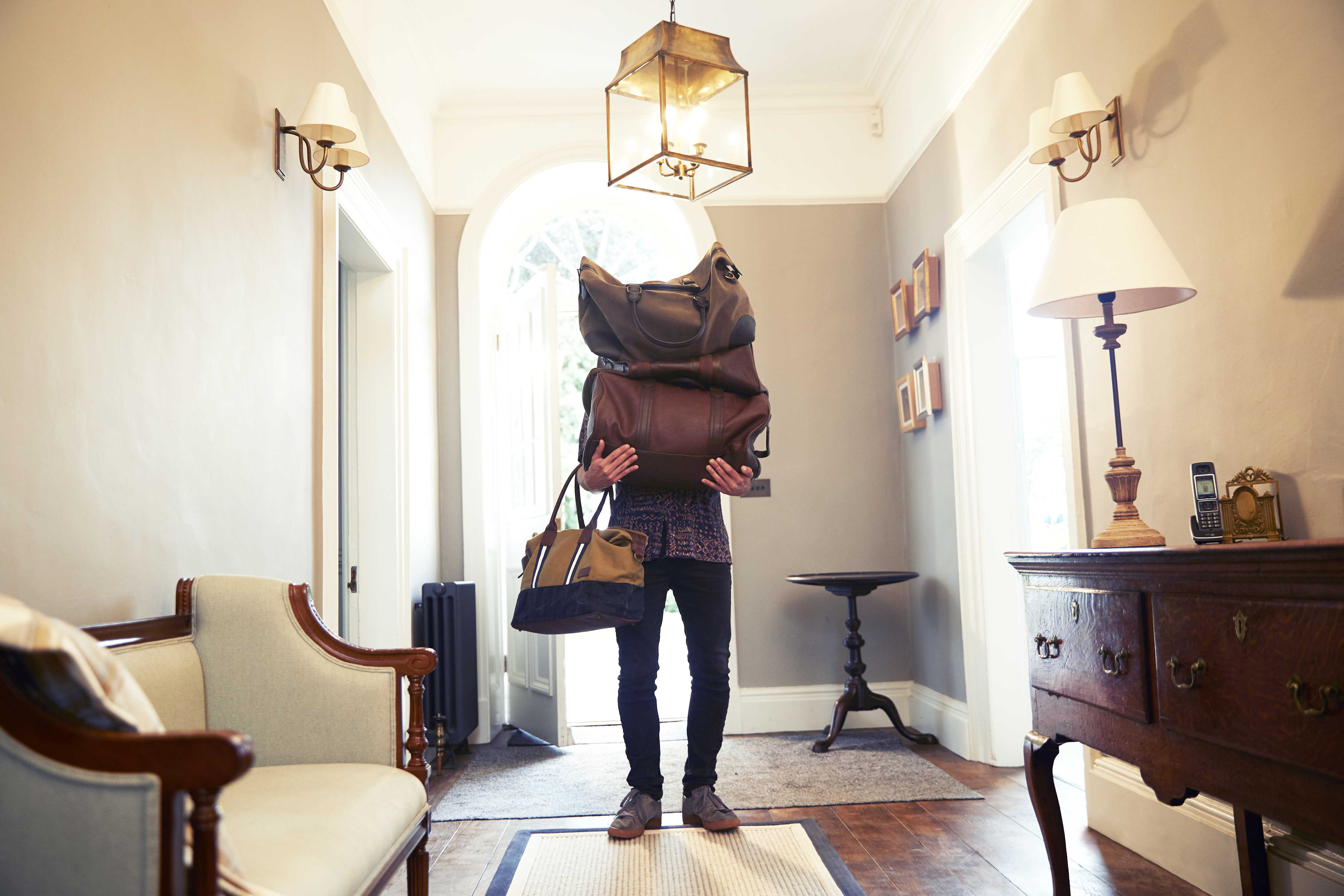Man entering a beautiful hallway holding luggage covering his face and upper body